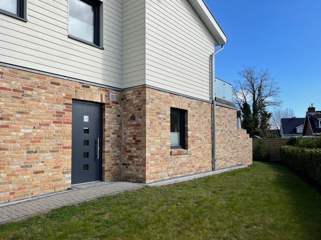 APPARTO Grömitz – Außenansicht des Hauses mit Klinker- und Holzfassade, Eingangstür und Rasenfläche