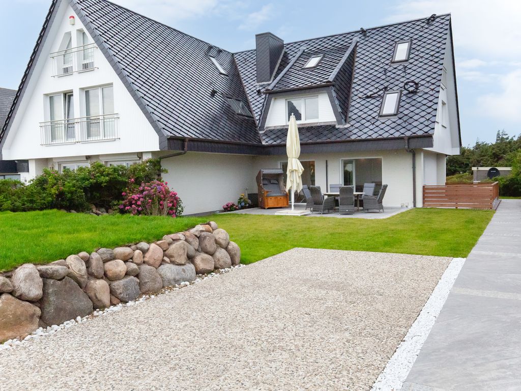 Haus am Meer in Wenningstedt-Braderup auf Sylt – weißes Friesenhaus mit dunklem Schieferdach, Terrasse und Rasenfläche hinter einer Feldsteinmauer