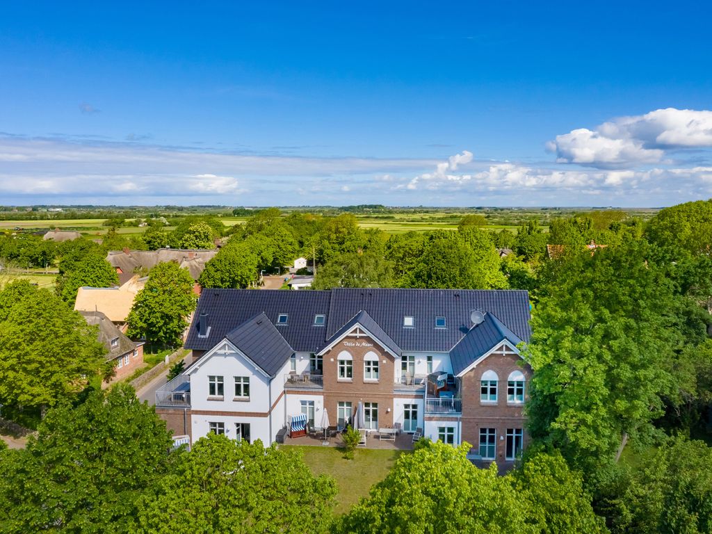 Villa de Meere Nieblum – Luftbild des weiß-roten Hauses mit Terrassen, umgeben von alten Bäumen und Marschland