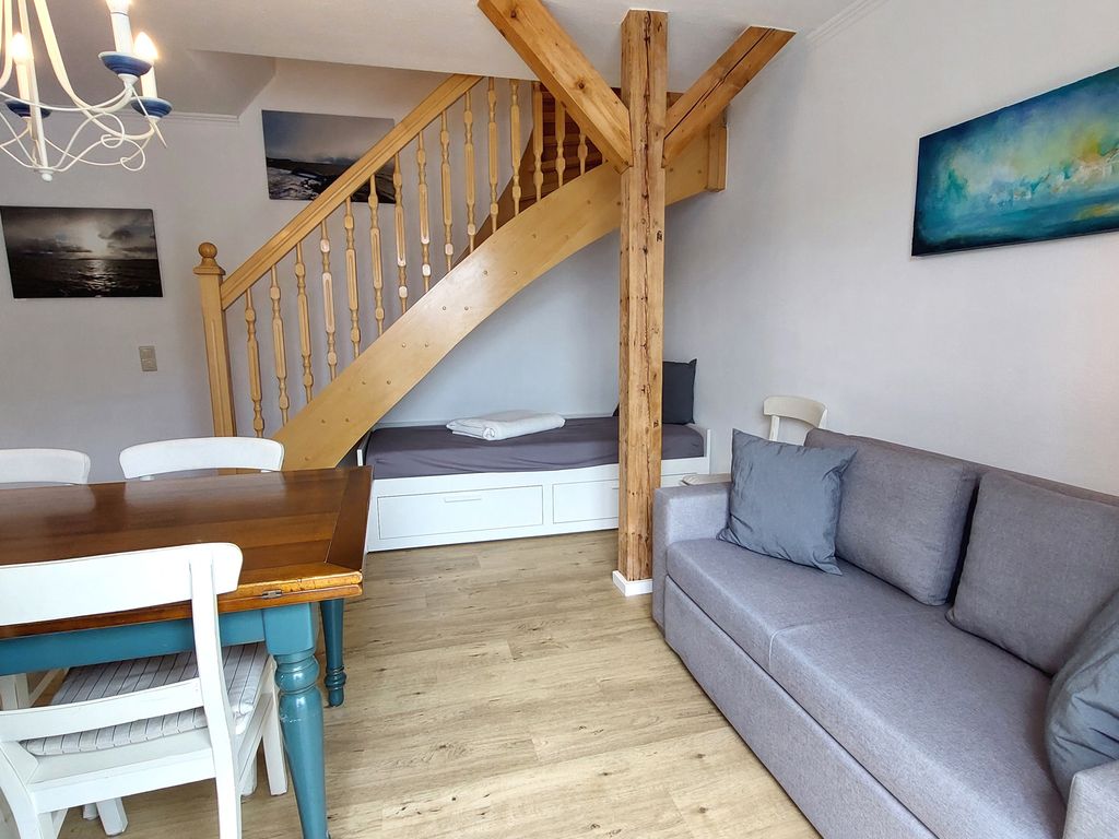Altes Postamt Binz – Wohnbereich mit geschwungener Holztreppe zur Galerie und Sofa