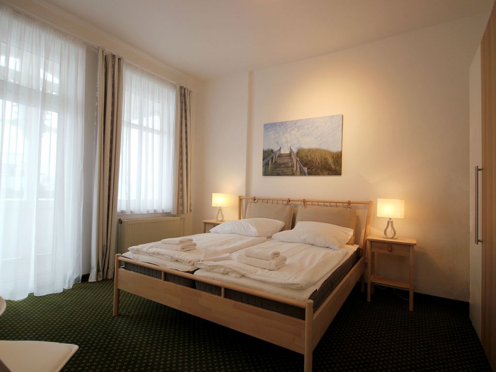 Haus Felicitas Binz – Schlafzimmer mit Holzbett, Nachttischlampen und Strandbild