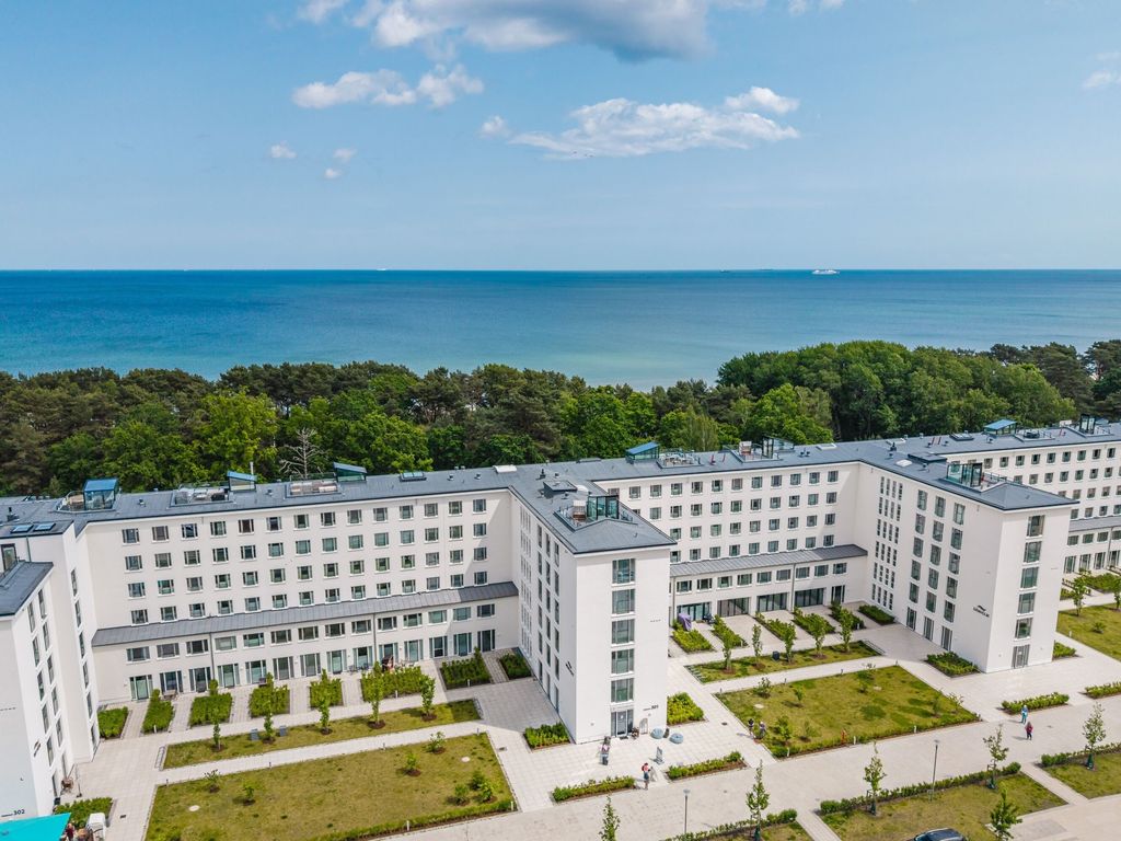 Haus Mönchgut Prora – Luftbild der weißen Anlage mit begrünten Innenhöfen, dahinter Kiefernwald und Ostsee