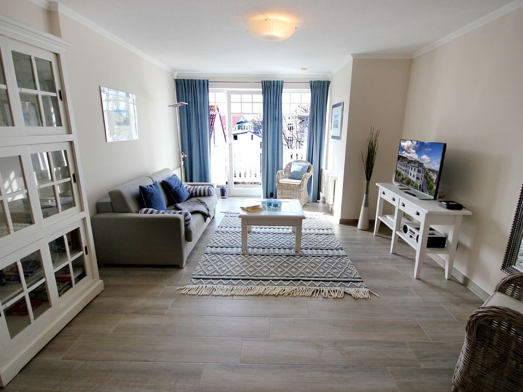 Villa Laetitia Binz – heller Wohnraum mit Sofa, blauen Vorhängen und Zugang zum Balkon