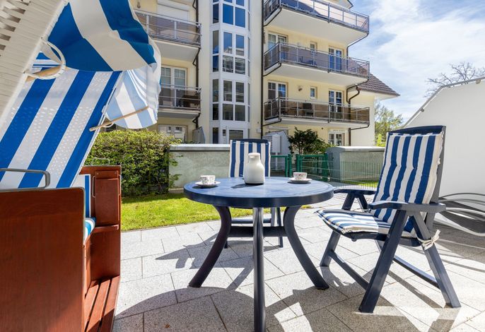 Haus am Kurpark 1 Baabe – Terrasse mit Strandkorb und Sitzgruppe vor dem gelben Apartmenthaus