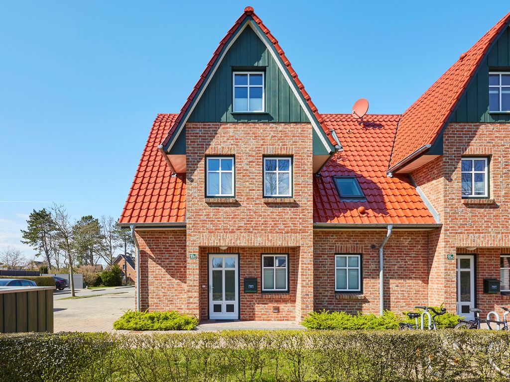 Haus Paula Wyk – rotes Backsteinhaus mit rotem Ziegeldach, grünem Giebel und Heckenvorgarten