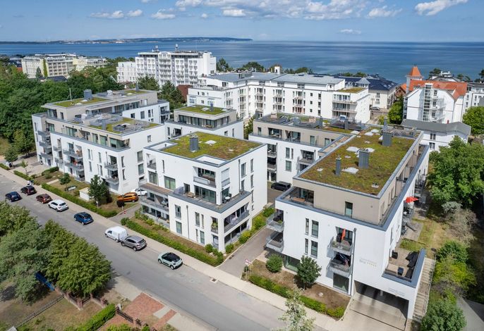 DünenResort Binz – Luftbild der weißen Neubau-Häuser mit begrünten Dächern, dahinter die Ostsee