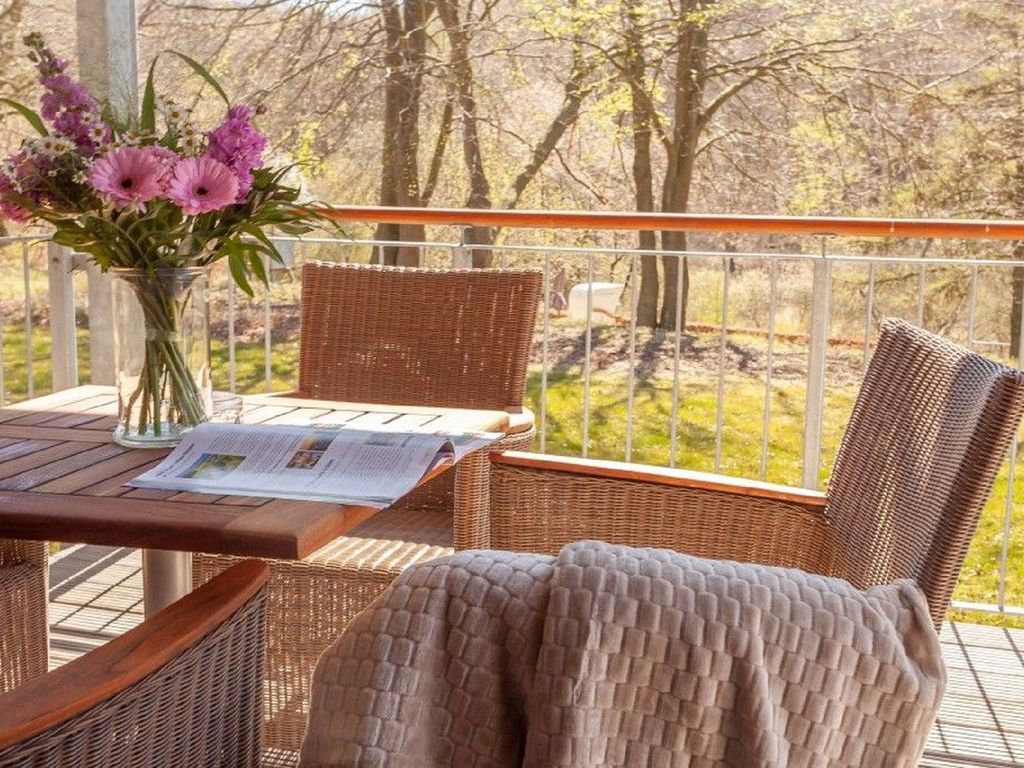 Haus Fore Lohme – Balkon mit Korbmöbeln und Blick auf Wiese und Baumbestand