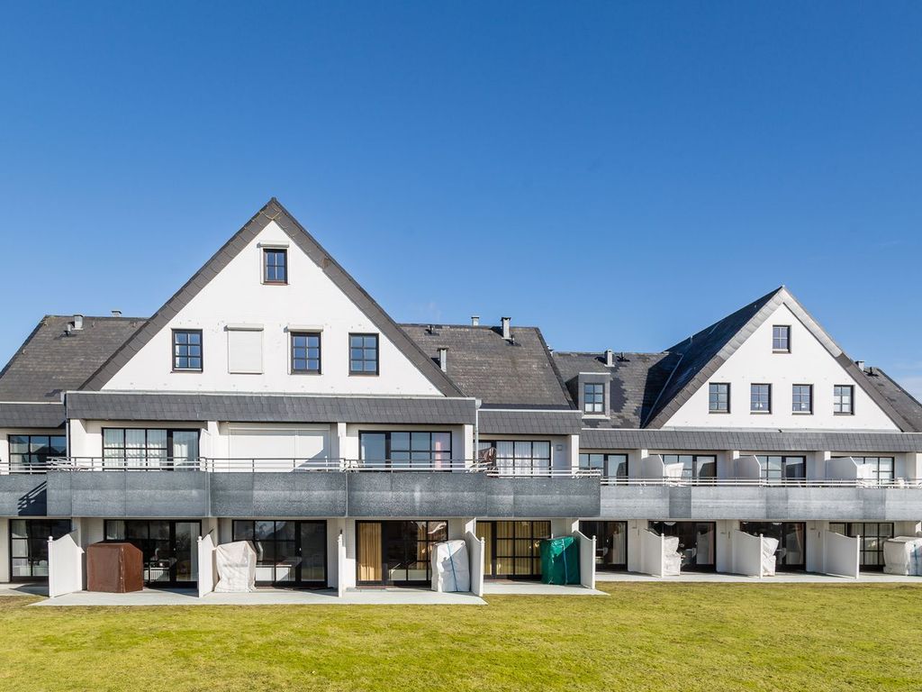 Haus Atlantik in Wenningstedt auf Sylt – weiße Apartmentanlage mit Giebeln, umlaufenden Terrassen und Strandkörben an der Rasenfläche