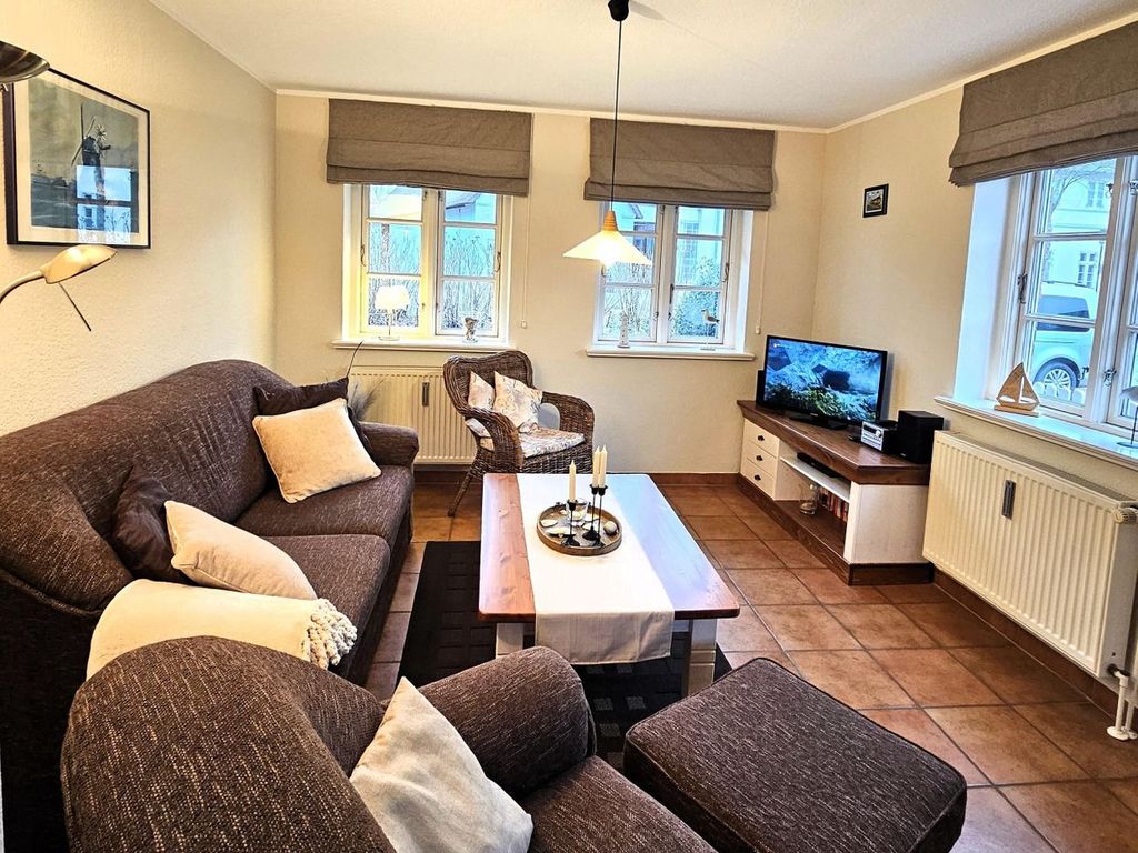 Gemütliches Wohnzimmer mit Sofa, Sessel und Fernseher.