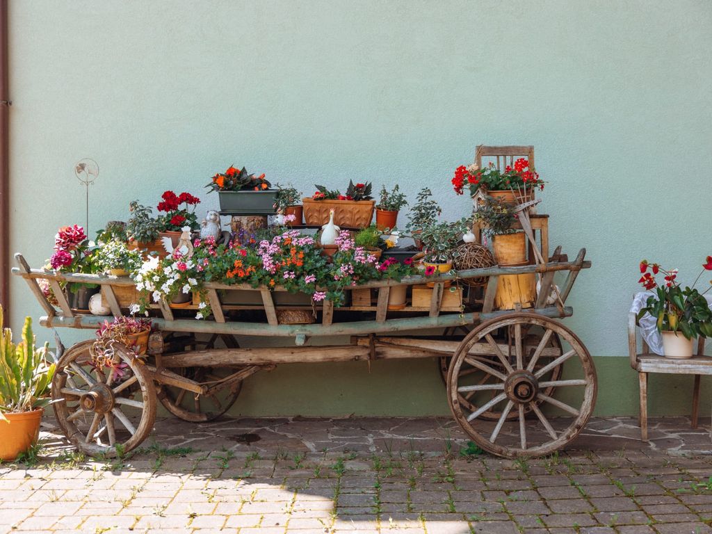 Ein liebevoll dekorierter Holzwagen mit bunten Blumen vor dem Bauernhof.