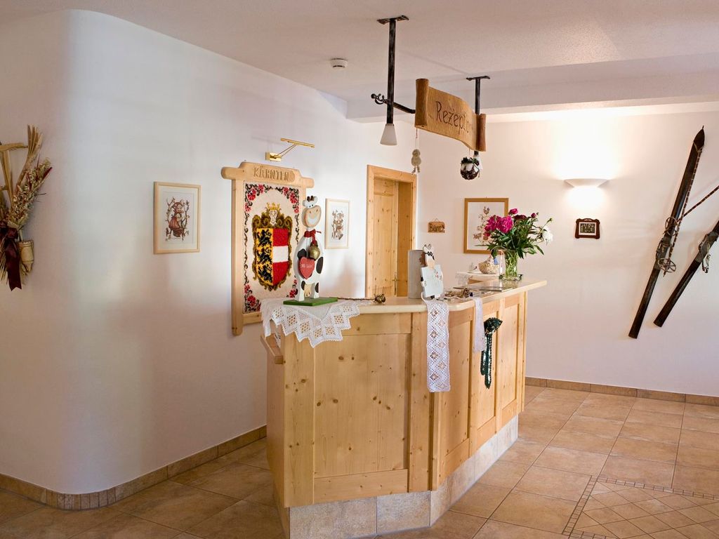 Der Empfangsbereich des Bauernhofs mit einer Rezeption aus hellem Massivholz, dekoriert mit traditionellen Skiern und dem Kärntner Wappen.