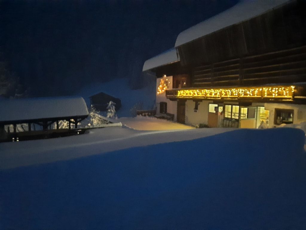 Der verschneite Bauernhof am Abend mit stimmungsvoll beleuchteten Balkonen und einer dicken Schneedecke.