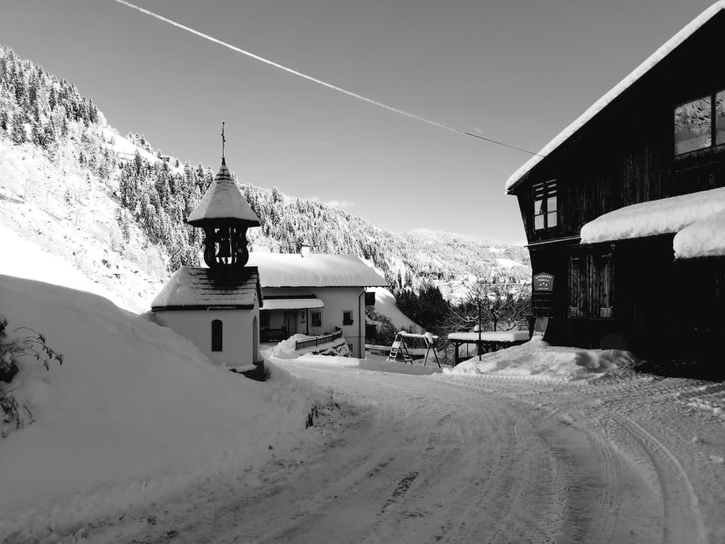 Der verschneite Bauernhof mit einer kleinen Kapelle und einer Schaukel im Winter.
