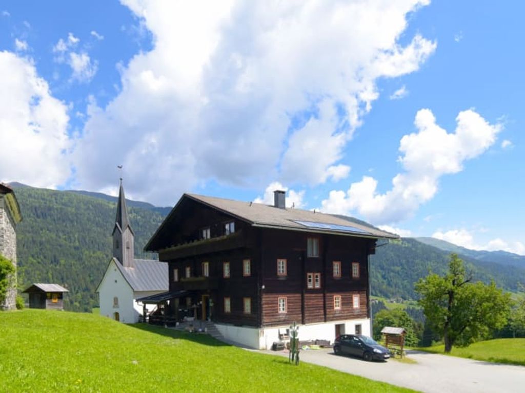 Der einladende Bauernhof inmitten von grünen Wiesen mit Blick auf eine idyllische Kirche und die Lesachtaler Bergwelt.