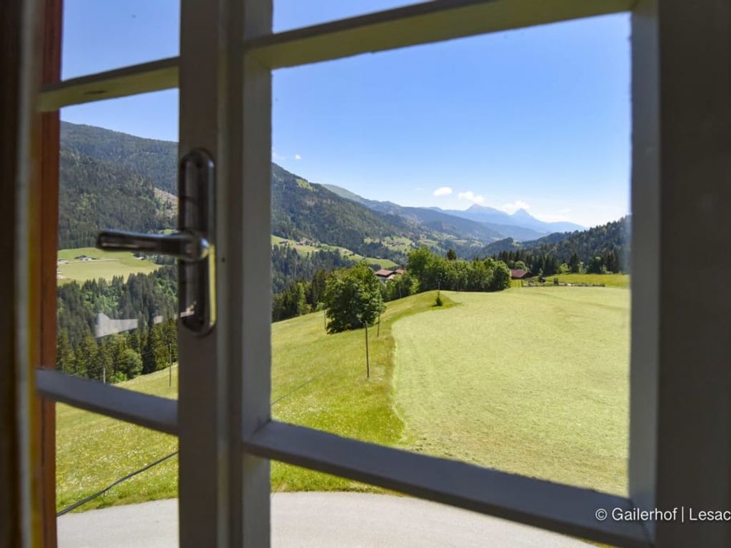 Blick durch das Fenster des Bauernhofs auf die idyllischen grünen Wiesen und die beeindruckende Lesachtaler Bergwelt.