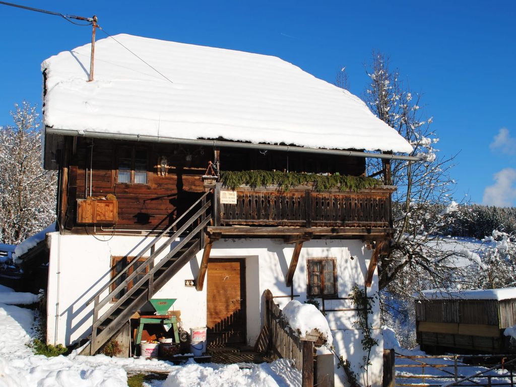 Die verschneite Fassade des Bauernhofs mit Balkon und Außentreppe im Winter.