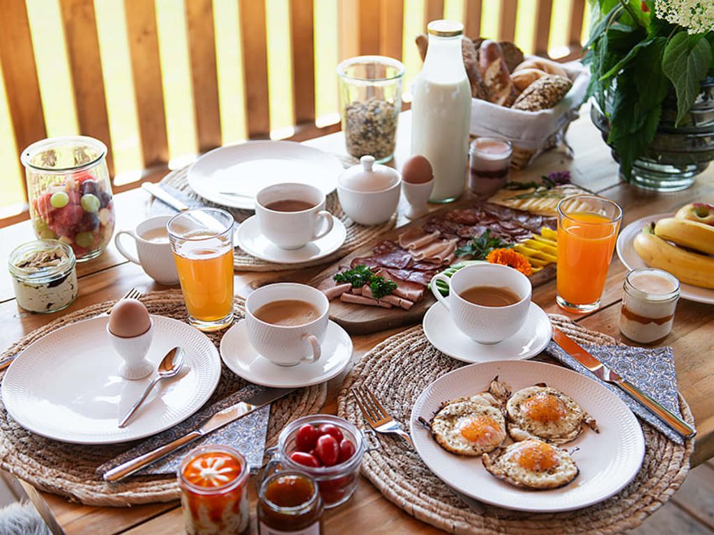 Reichhaltiges Frühstück auf der Terrasse des Chalets mit Spiegeleiern, Aufschnitt, Brot, Obst und Getränken.