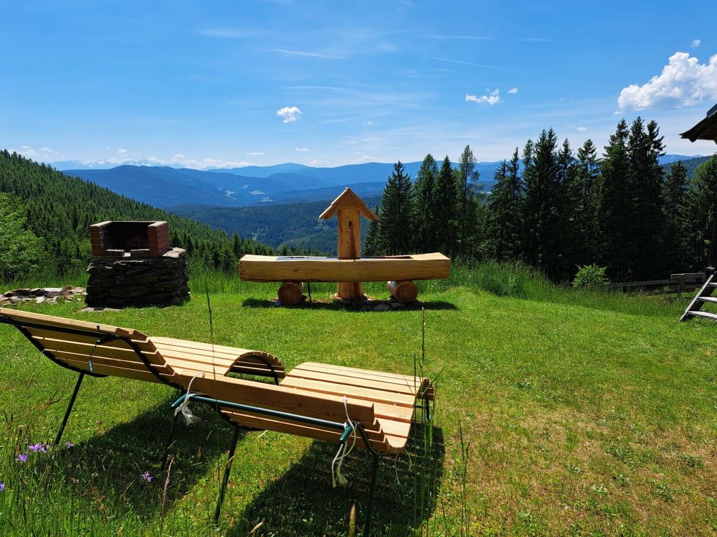 Die Alm bietet einen Grillplatz, einen Holzbrunnen und Liegestühle auf der Wiese mit Bergblick.