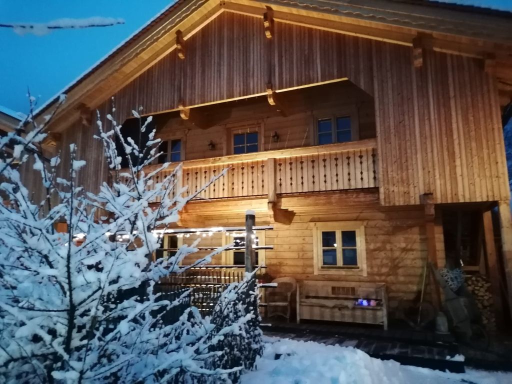 Der Hof von außen im Winter, mit beleuchtetem Holzbalkon und verschneiter Umgebung.