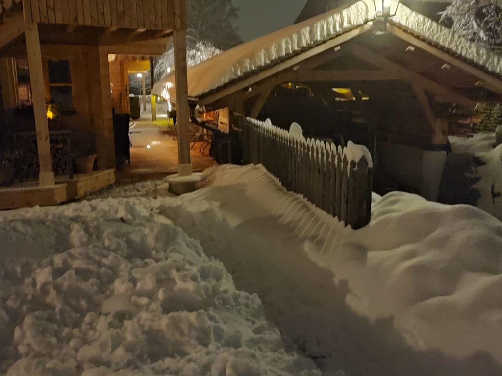 Der Hof im Winter bei Nacht, mit schneebedeckten Wegen und einem beleuchteten Holzcarport.