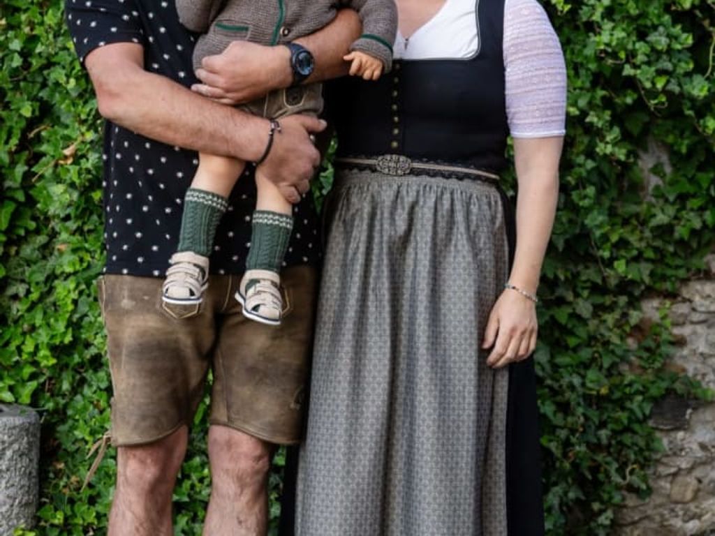 Die Gastgeberfamilie des Bauernhofs in traditioneller Tracht vor einer mit Efeu bewachsenen Wand.