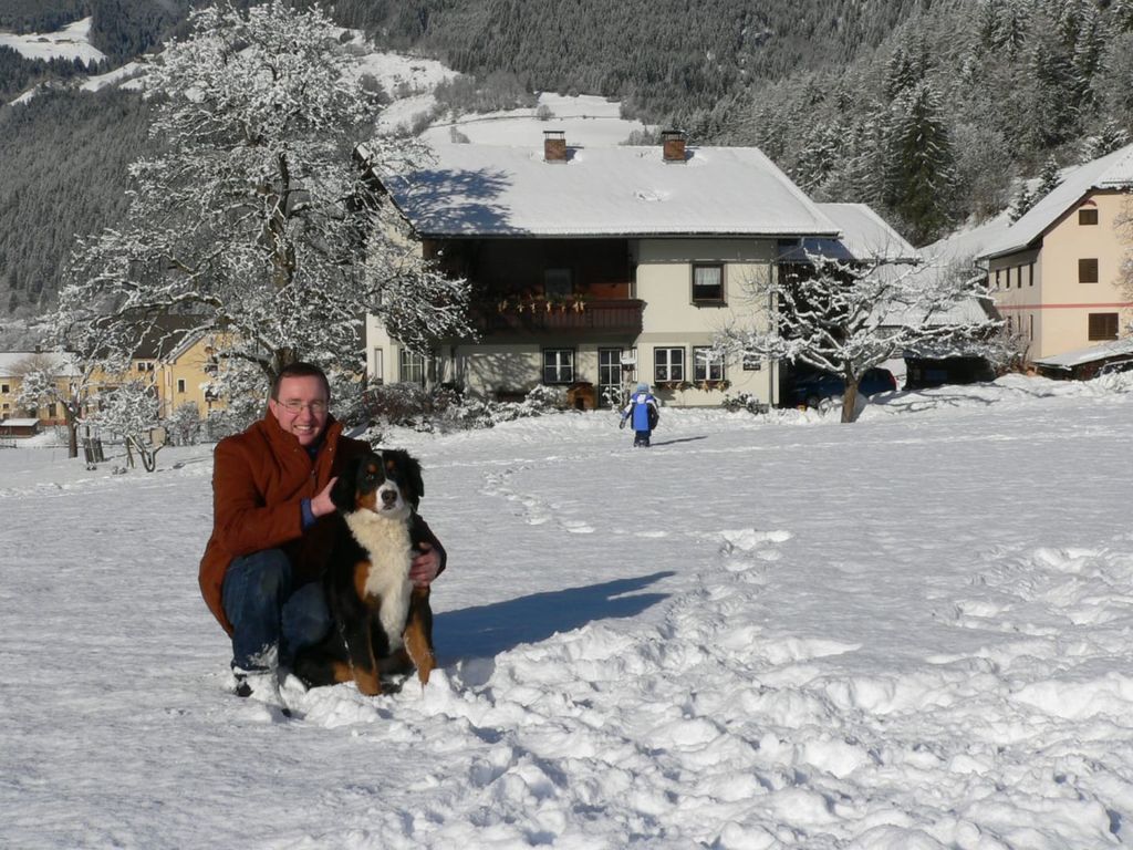 Der Bauernhof in einer verschneiten Winterlandschaft, mit einem Hofhund und einem Kind im Schnee.
