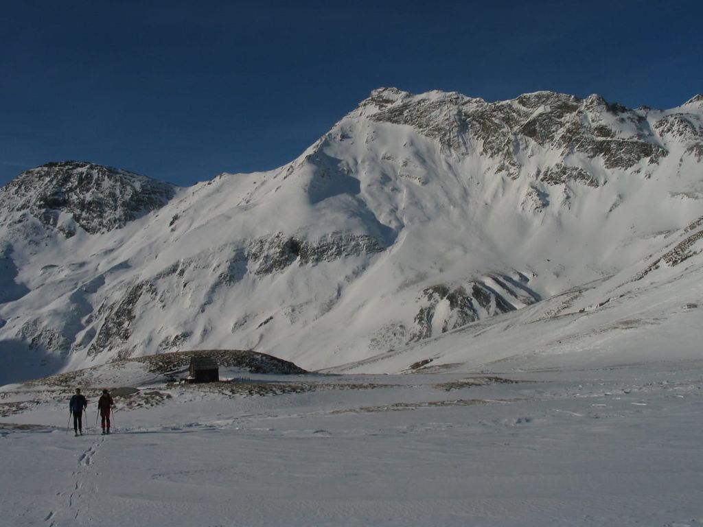 Weite schneebedeckte Berglandschaft mit Winterwanderern und einer kleinen Hütte, die Teil der Bergwelt rund um den Bauernhof ist.