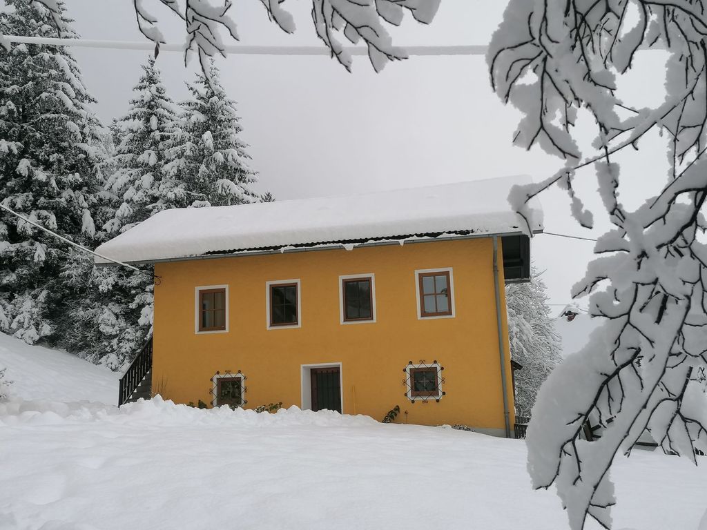 Der gelbe Bauernhof im Winter, umgeben von Schnee und verschneiten Bäumen.