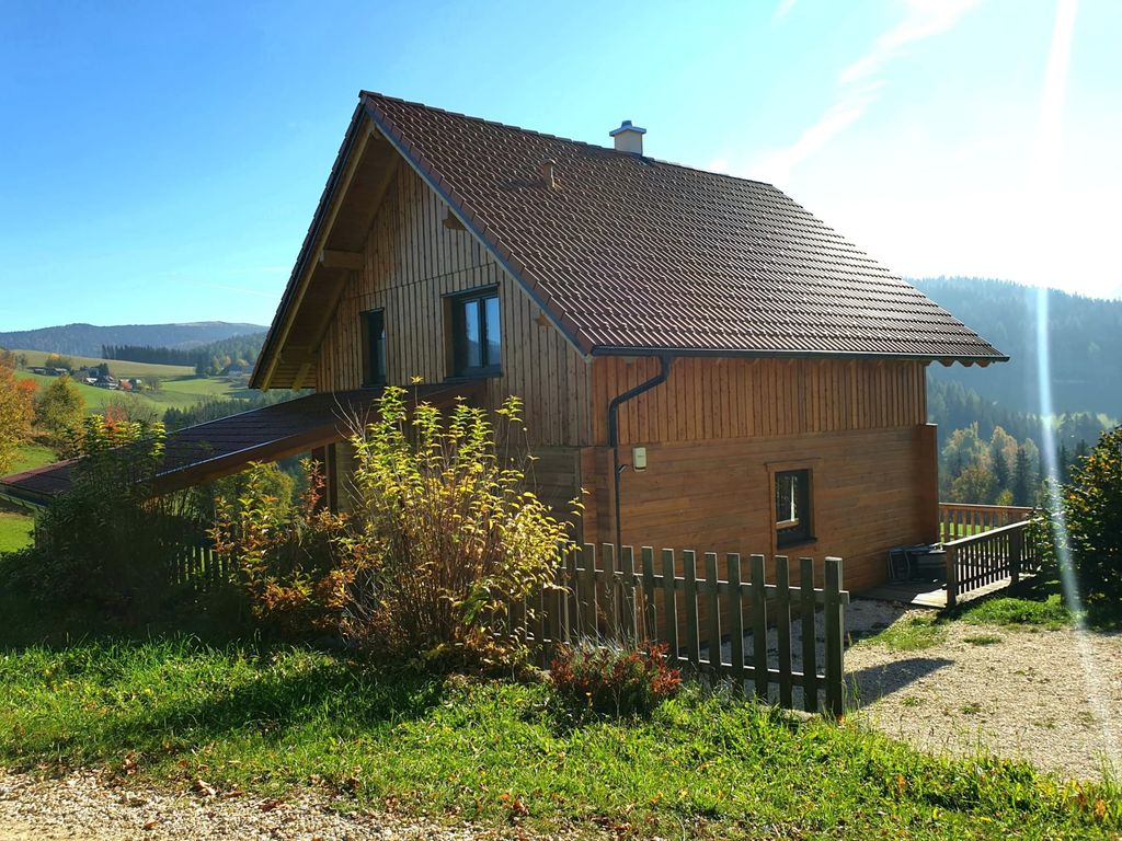 Das Ferienhaus in Holzbauweise mit Terrasse und Blick auf die umliegende Hügellandschaft.