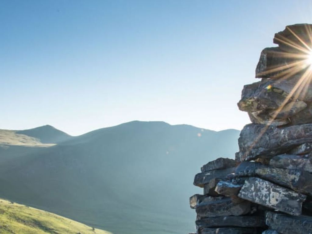 Ein Steinmännchen auf einem Berg mit Blick auf die grüne Hügellandschaft, ideal für Wanderungen vom Bauernhof aus.