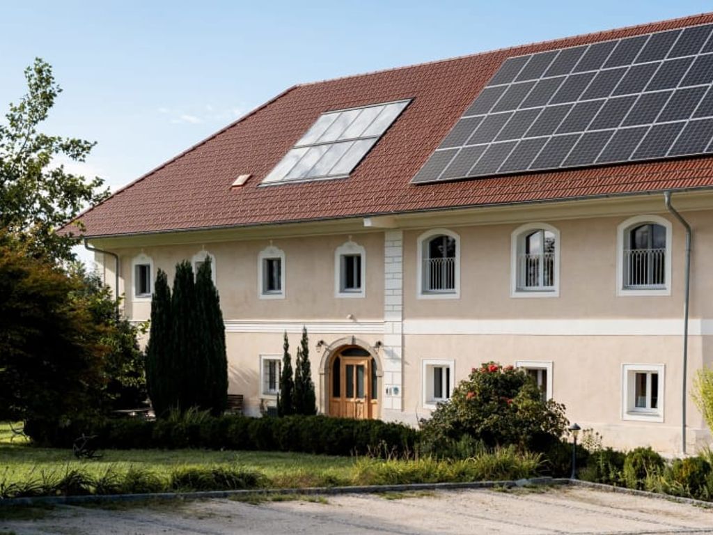 Das einladende Gebäude des Bauernhofs mit einem gepflegten, grünen Garten und modernen Solarmodulen auf dem Dach.