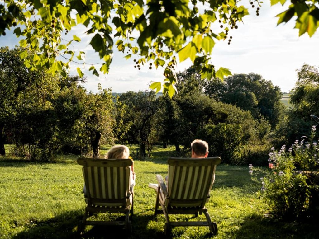 Der einladende Ruhegarten des Bauernhofs mit bequemen Liegestühlen unter schattigen Bäumen und weitem Blick ins Grüne.