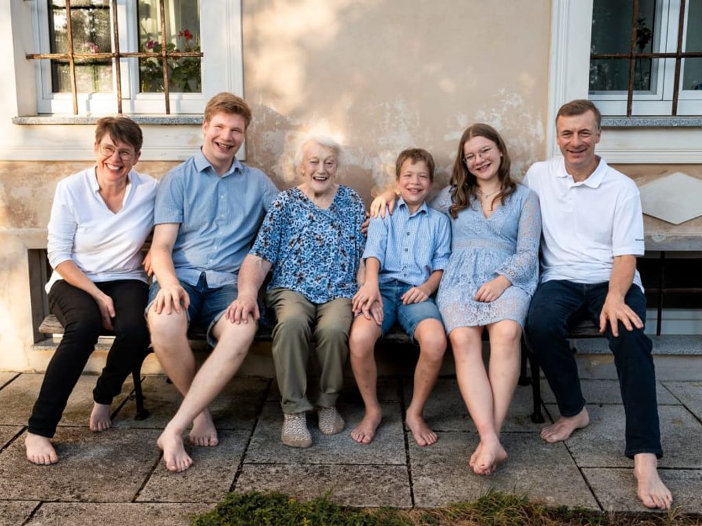 Die herzliche Gastgeberfamilie auf einer gemütlichen Holzbank vor dem Bauernhof.