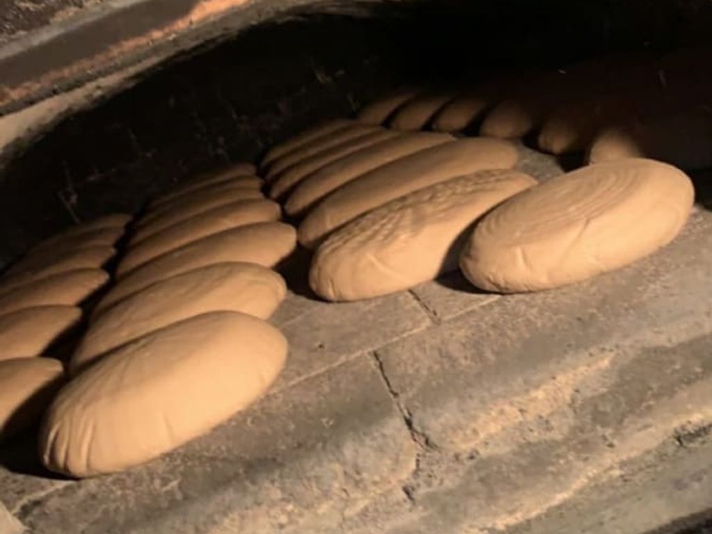 Frisch geformte Brotlaibe im traditionellen Steinofen des Bauernhofs.