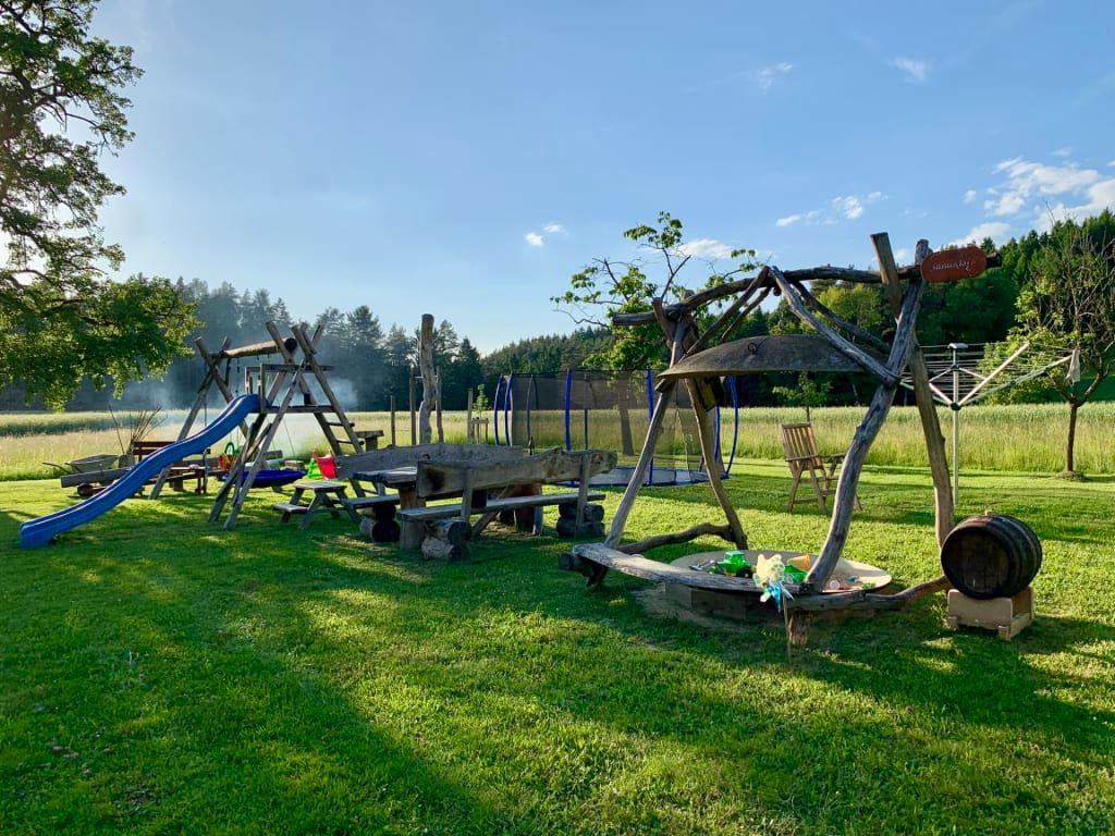 Der großzügige Garten des Bauernhofs mit einem einladenden Kinderspielplatz samt Rutsche, Trampolin und gemütlicher Holzsitzgruppe.