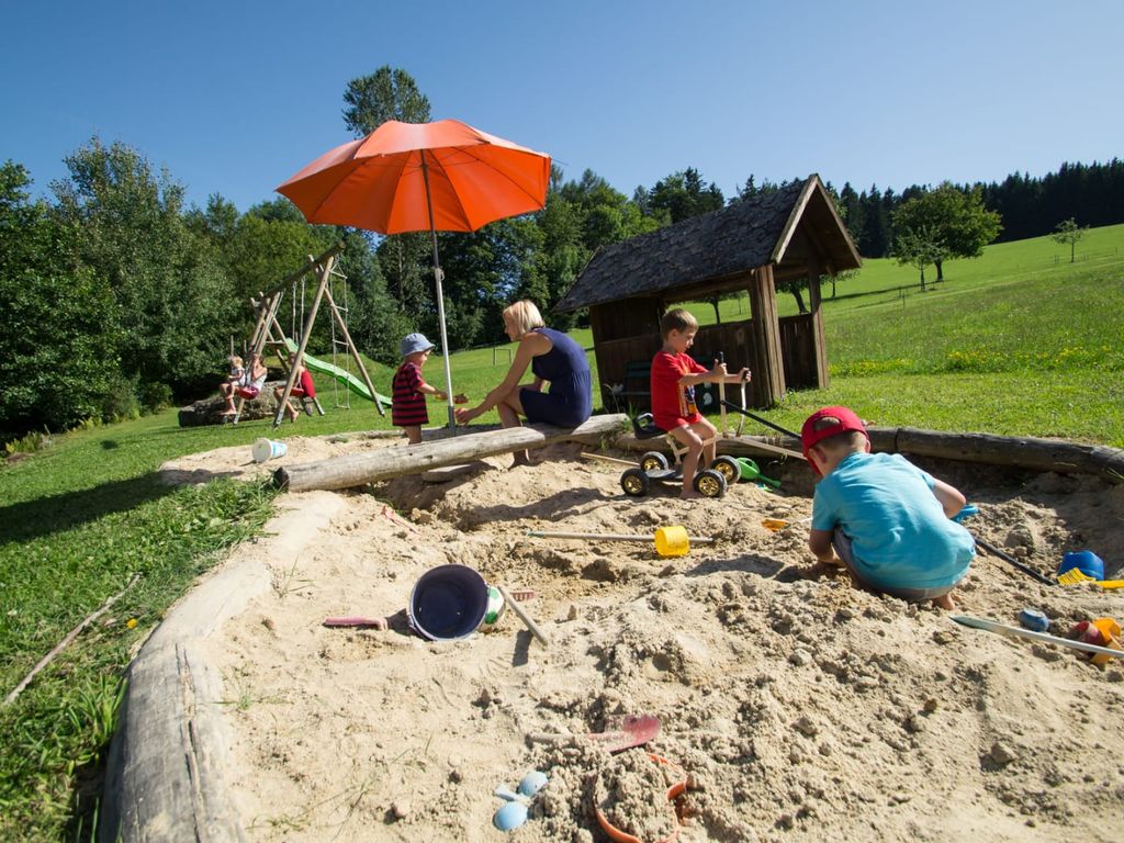 Der Kinderspielplatz des Bauernhofs umfasst einen Sandkasten mit Sonnenschirm, eine Schaukel und ein Holzspielhaus.
