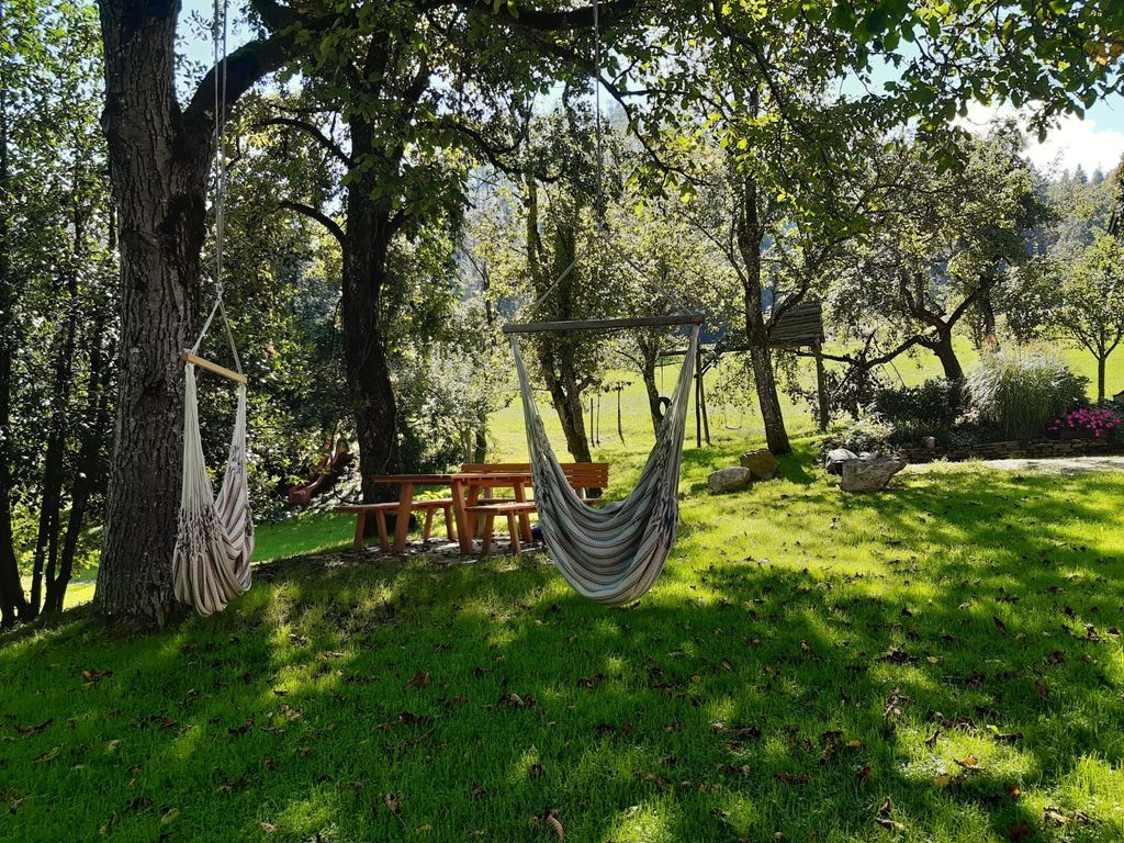 Der Garten des Bauernhofs mit Hängesesseln und einem Picknicktisch unter Bäumen.