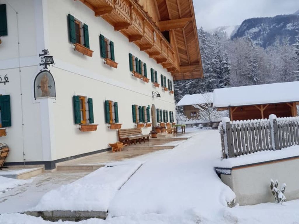 Außenansicht des Bauernhofs im Winter, mit Schnee bedeckt, traditionellen Holzbalkonen und grünen Fensterläden.