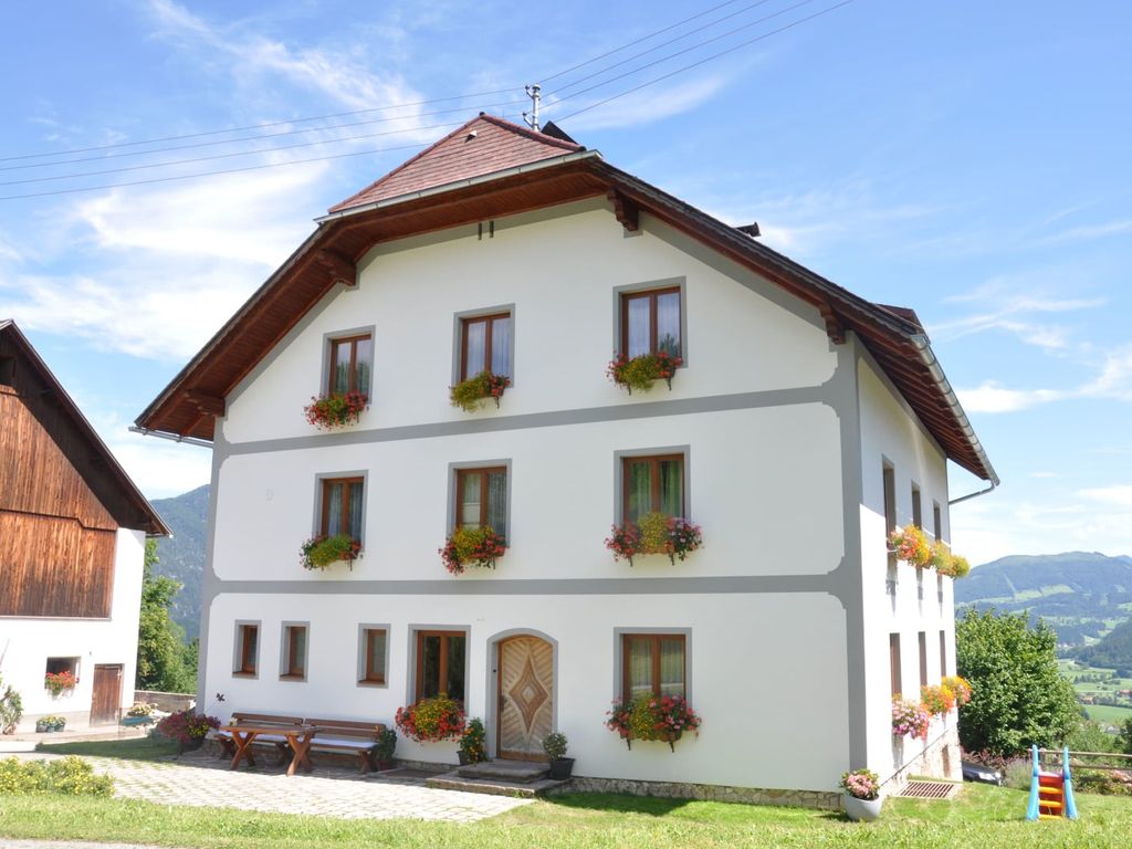 Das Bauernhofgebäude mit blumengeschmückten Fenstern, Sitzbänken im Freien und einer kleinen Rutsche auf der Rasenfläche.