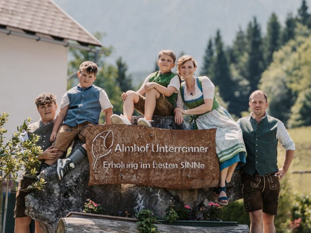 Die Familie des Bauernhofs Almhof Unterranner begrüßt Sie in traditioneller Kleidung am Hofschild.