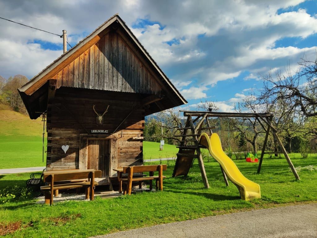 Spielplatz mit Rutsche und Schaukeln sowie eine Holzhütte mit Sitzgelegenheiten auf dem Bauernhof.