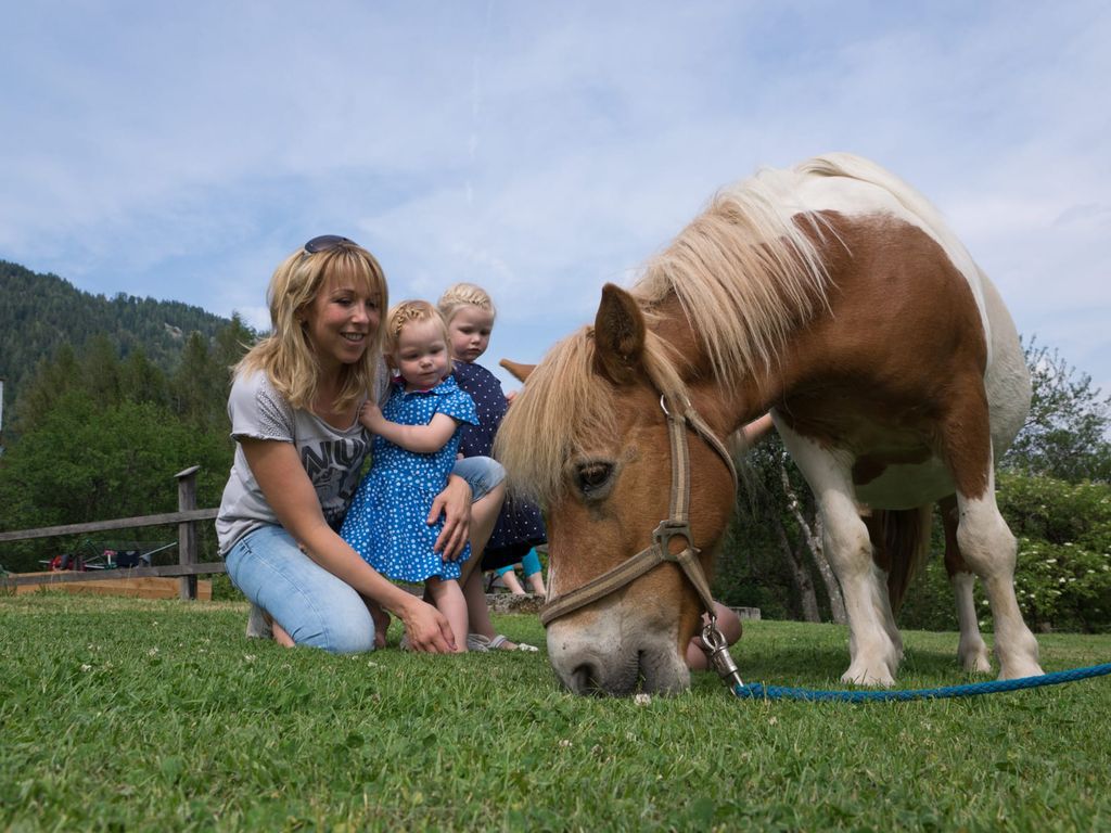 Eine Frau mit zwei Kindern und einem grasenden Pferd auf der Wiese des Bauernhofs.