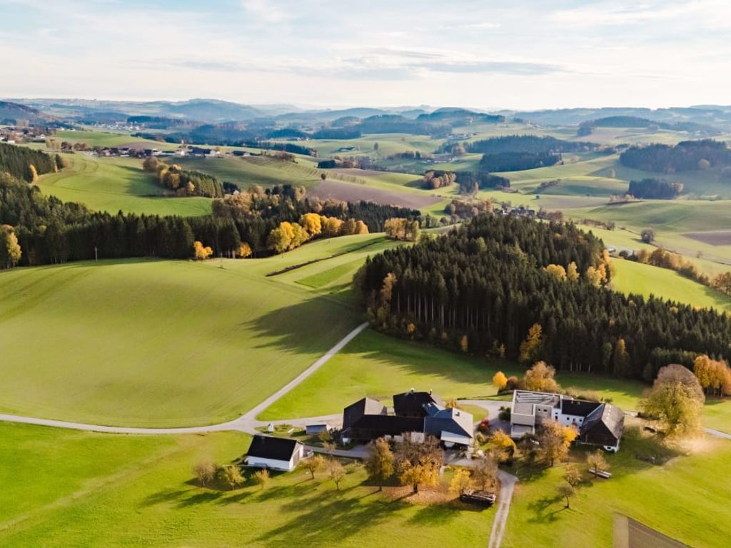 Der Bauernhof liegt inmitten der grünen Hügellandschaft des Nördlichen Mühlviertels, umgeben von Feldern und Wäldern.