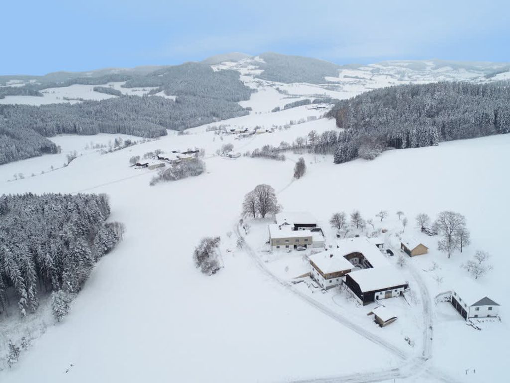 Der Bauernhof in einer verschneiten Winterlandschaft des Nördlichen Mühlviertels, umgeben von Feldern und Wäldern.