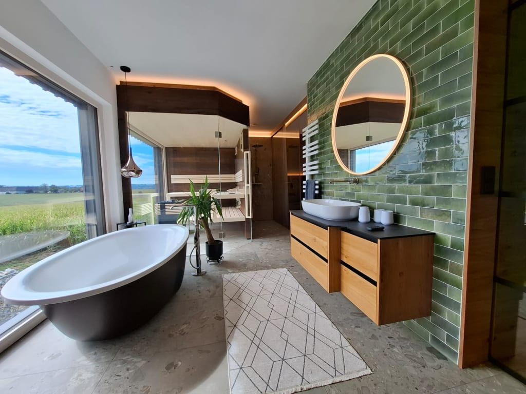 Das luxuriöse Badezimmer des Ferienhauses mit freistehender Badewanne, einer Sauna und Panoramablick ins Grüne.