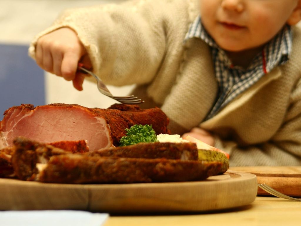 Ein Kind greift zu einem Stück Braten, serviert auf einem Holzbrett auf dem Bauernhof.