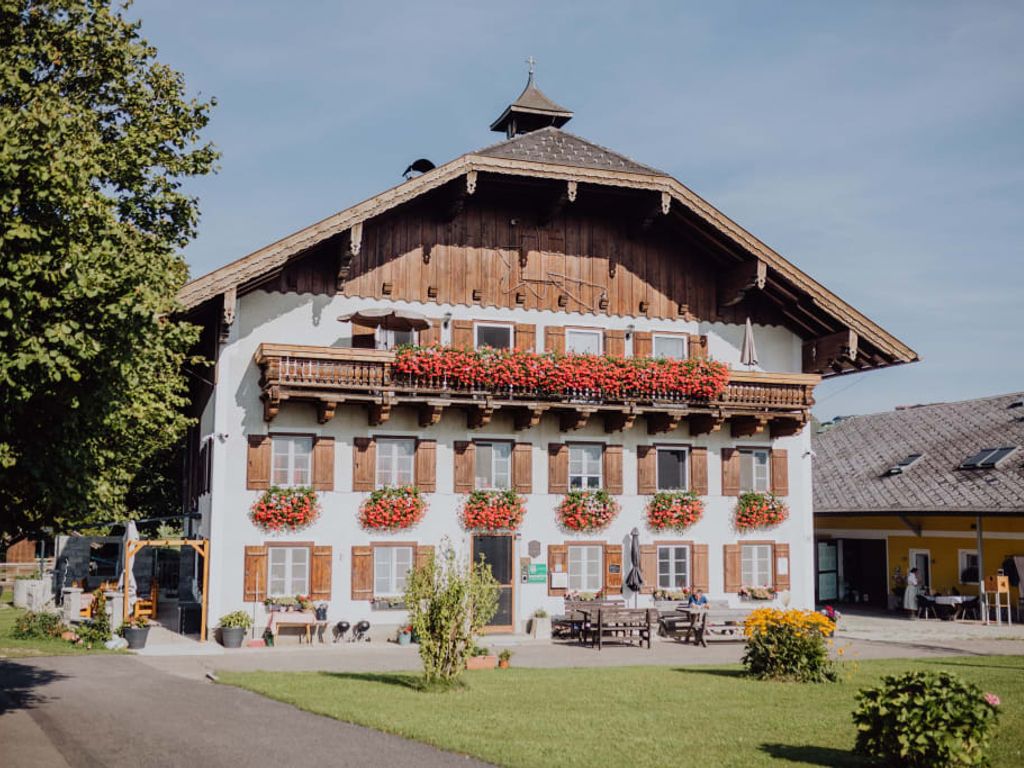 Der Bauernhof mit traditioneller Architektur, Holzbalkonen, Blumenkästen und einem Sitzbereich im Freien.