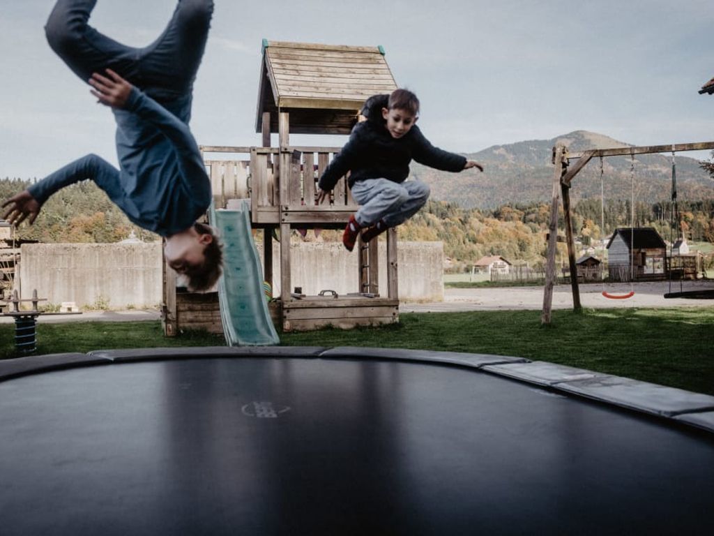 Kinder springen auf dem Trampolin des Bauernhofs, mit einem Spielplatz und Schaukeln im Hintergrund.