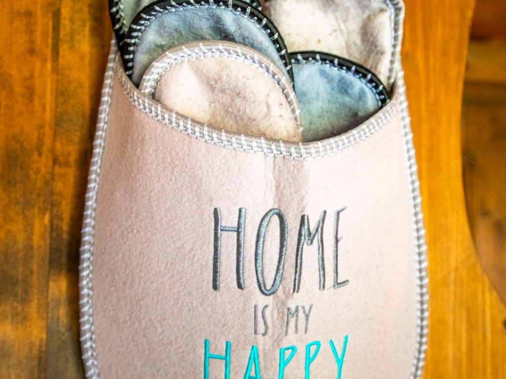 Pantoffeln für Gäste, präsentiert in einem Filzhalter mit der Aufschrift „HOME IS MY HAPPY PLACE“ im Bauernhof.