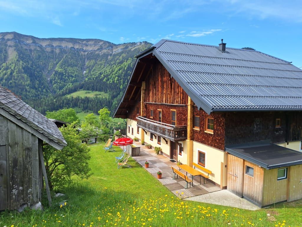Der Bauernhof von außen mit Terrasse, Picknicktisch, Liegewiese und Bergblick.